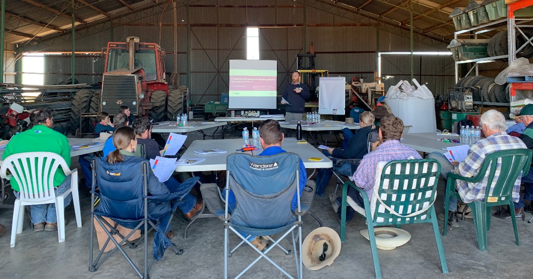 Beef producers sit in camp chairs at tables in a shed where Principal Agronomist, Stuart Buck, discusses the key principles to establishing perennial legumes in grass pastures.