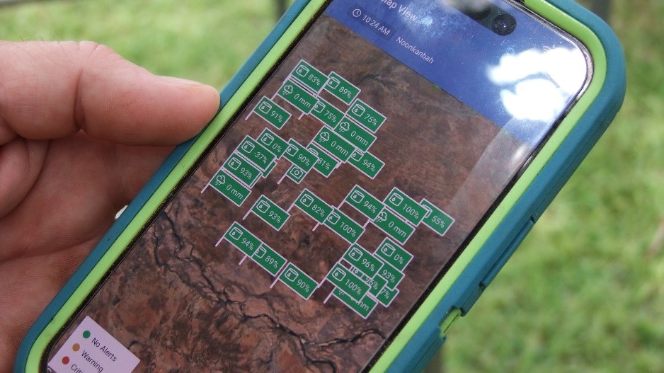 A person holding a mobile phone displaying the Farmbot app.