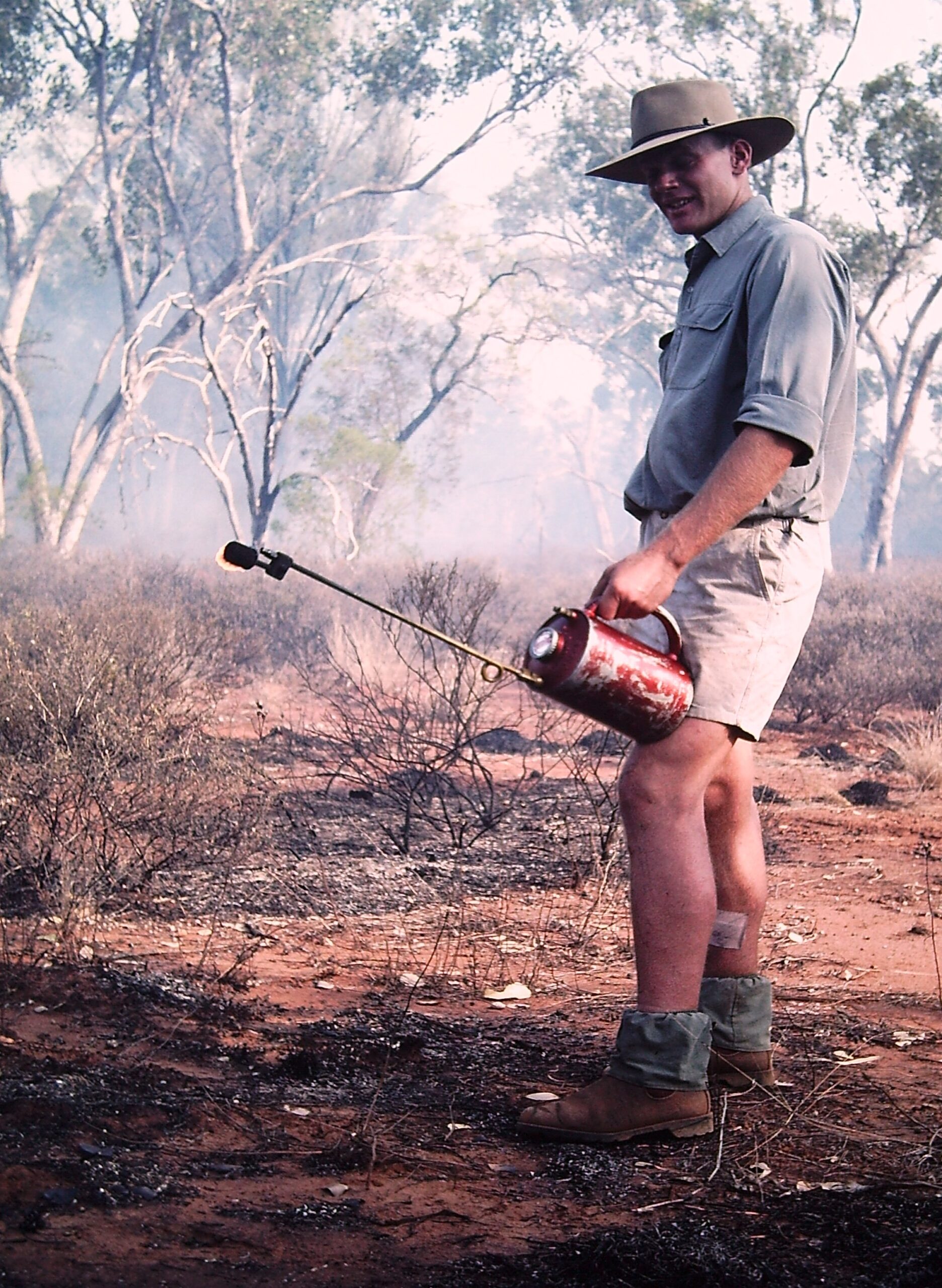 Man holding a drip torch conducting a controlled burn.