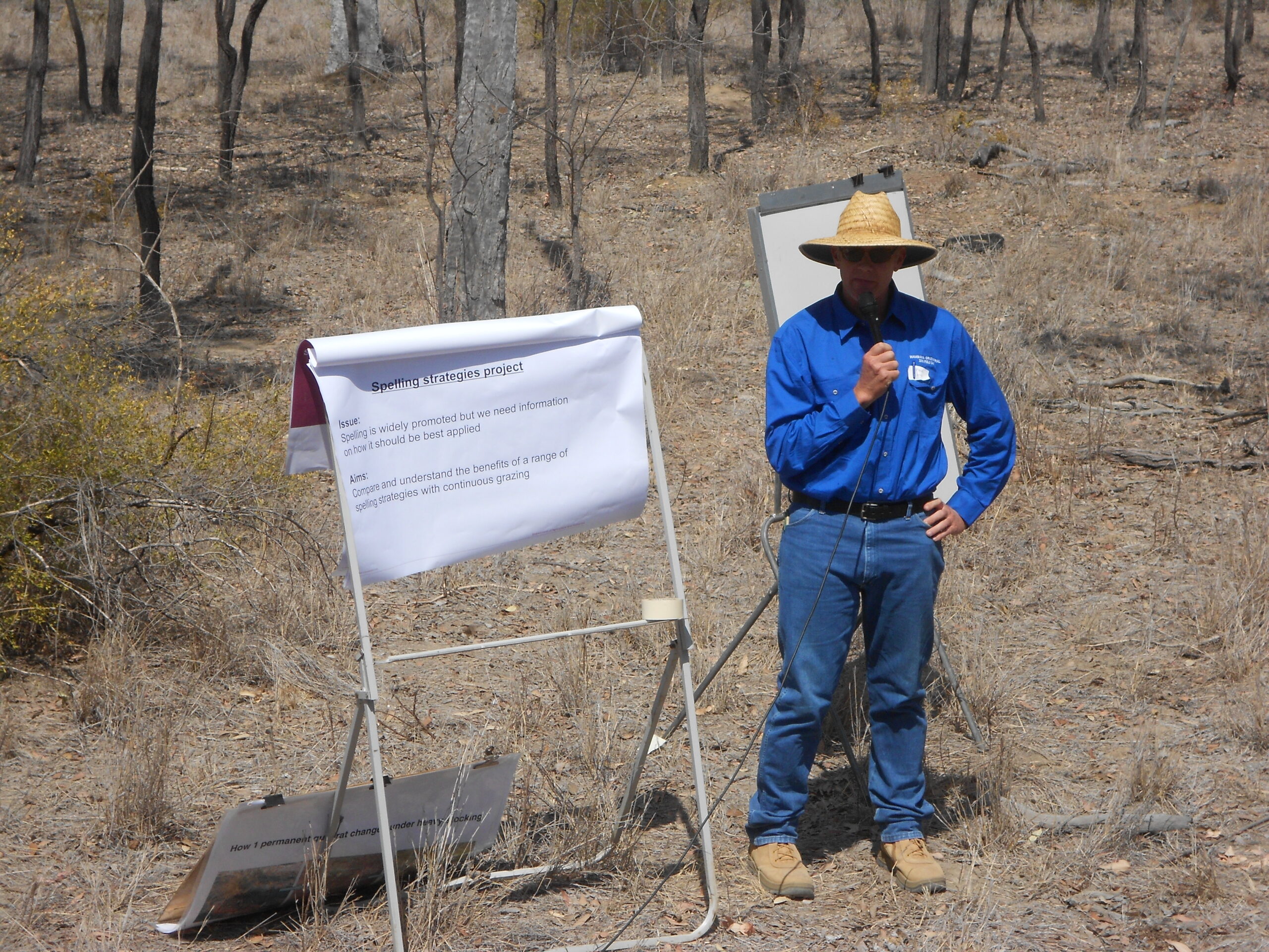 Man standing in front of a flip chart in a paddock speaking on a microphone.