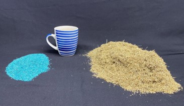 Photo showing on the left coated Callide Rhodes grass seed, in the middle a coffee cup for scale and on the right, a large pile of uncoated seed of the same variety.