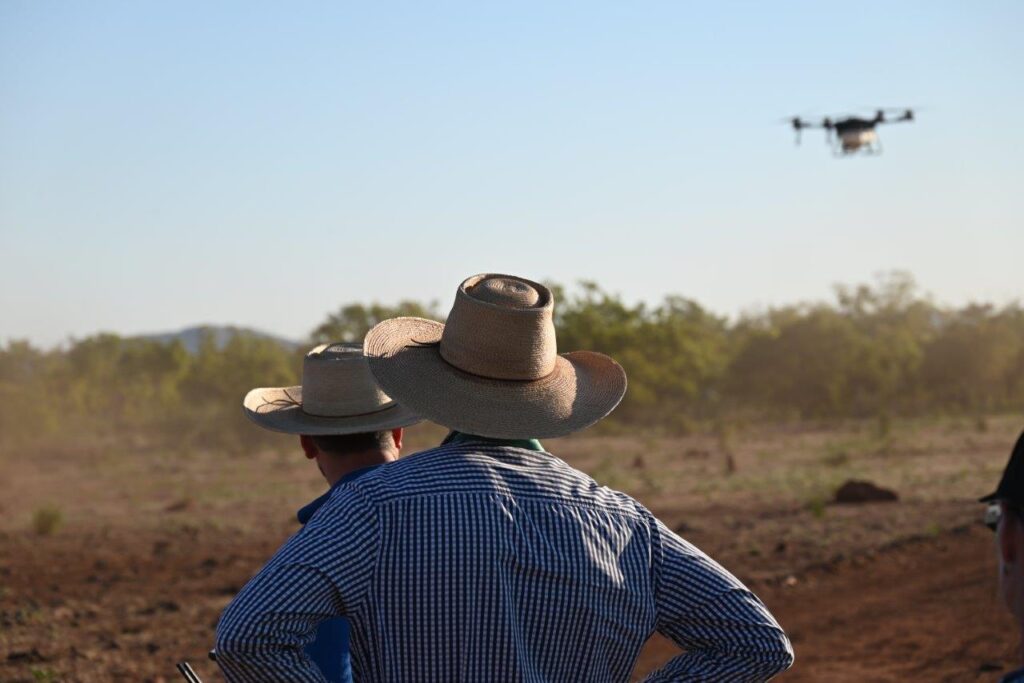 Photo of two people in a paddock watching a drone taking off.