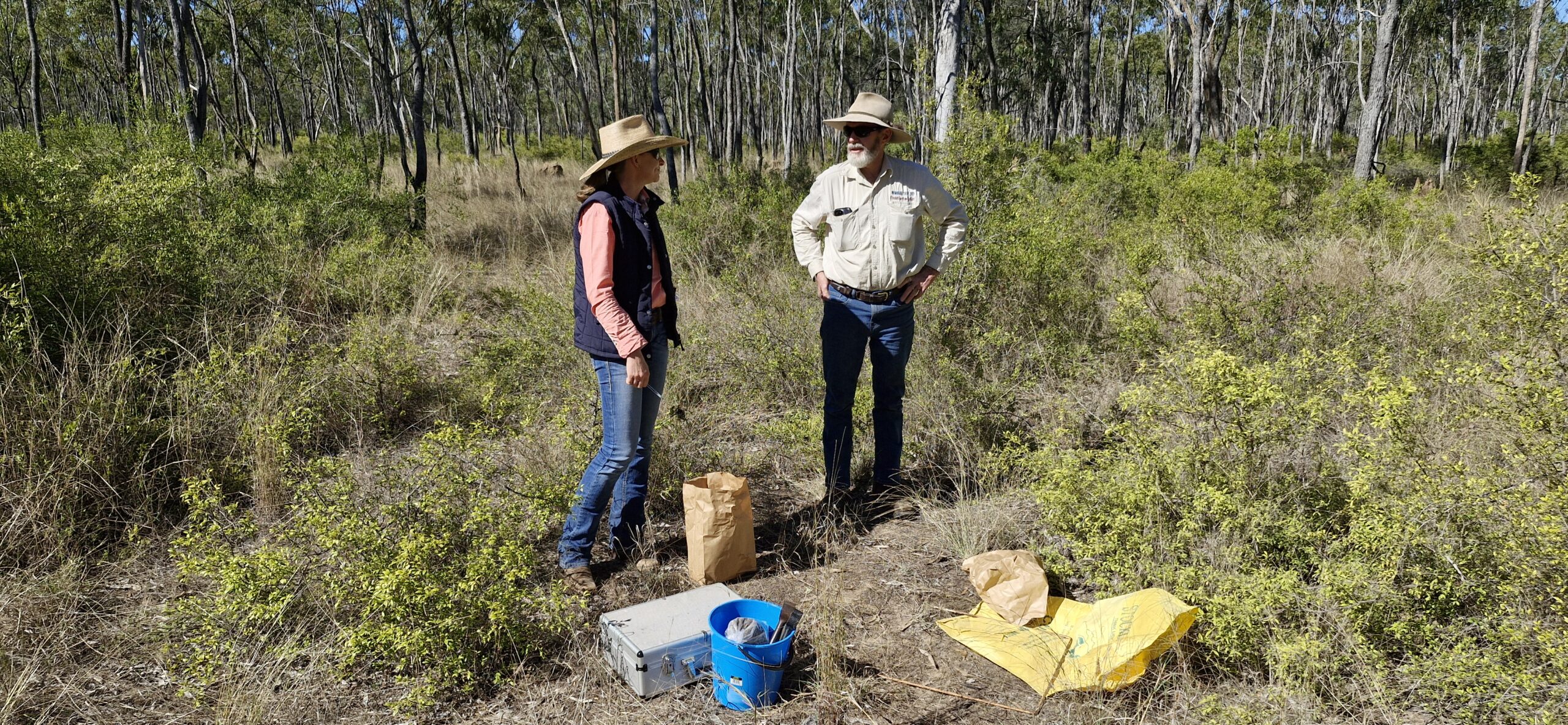 A man and woman standing in a paddock with materials needed to harvest and weigh grass.