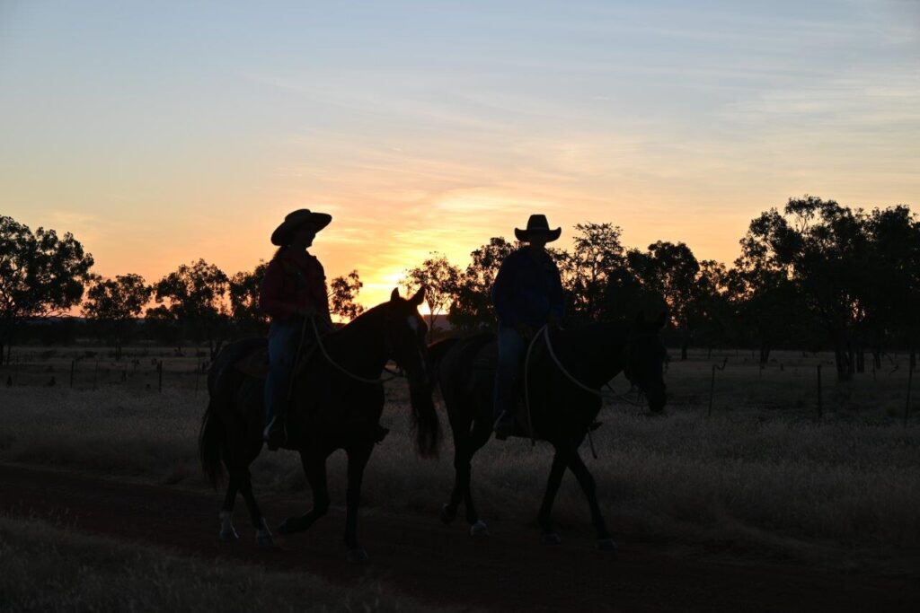 A photo of two people on horses in the sunset.