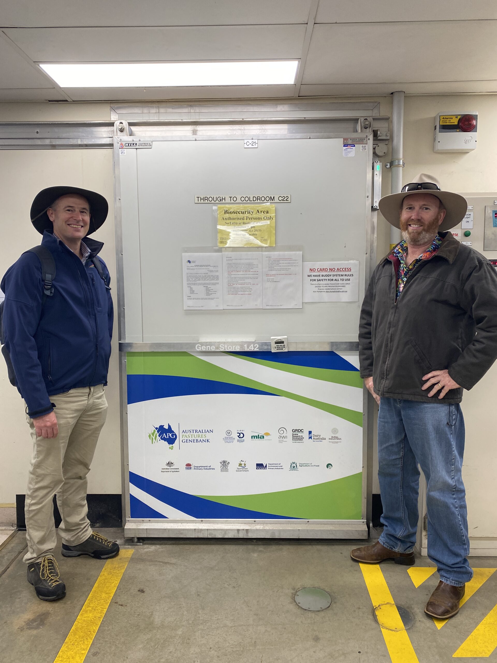 Two men standing either side of a door to a cold room.