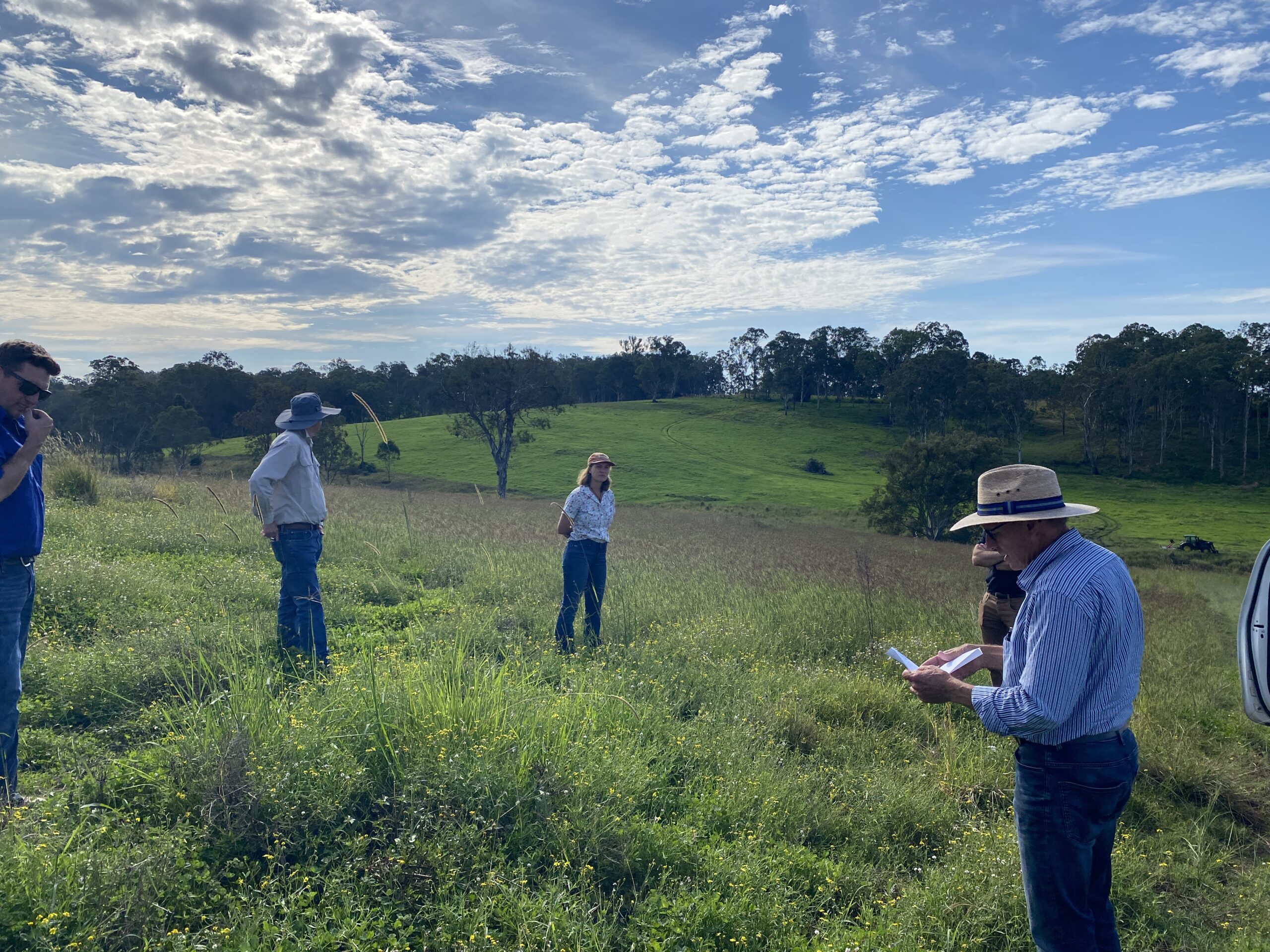 People standing in a paddock of green grass with a man on the left reading from some notes.