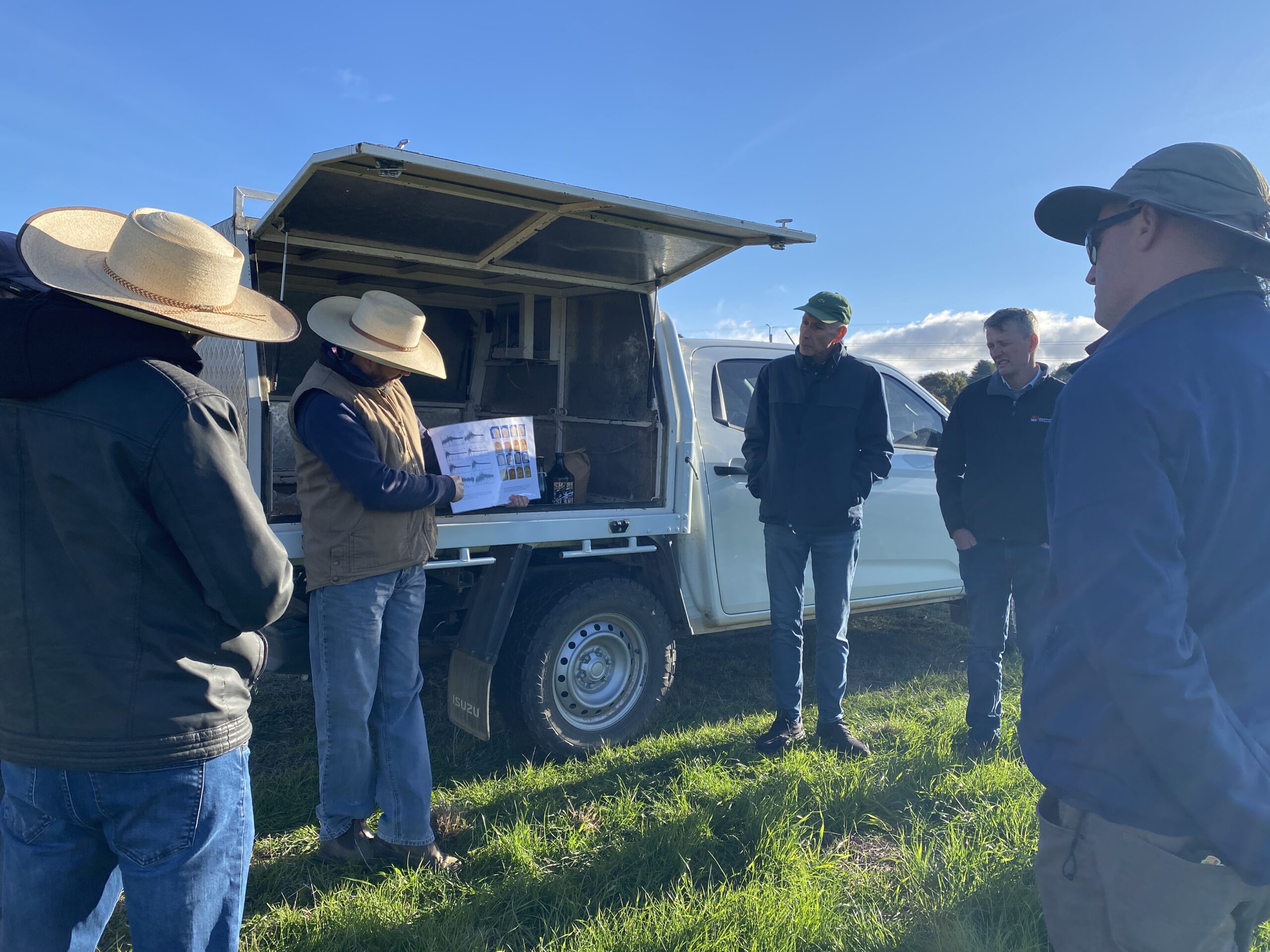 A man at the back of a ute in a paddock using a poster to explain trial results.