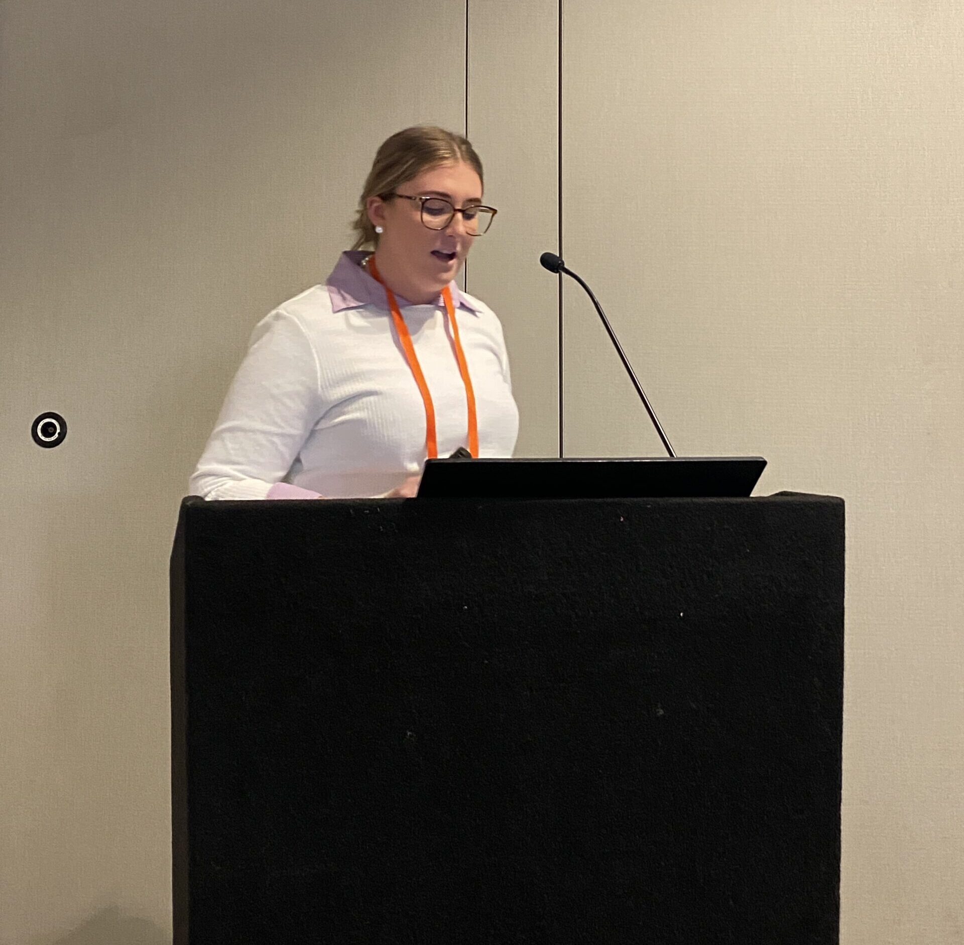Lady in a white jumper standing at a podium speaking into a microphone.