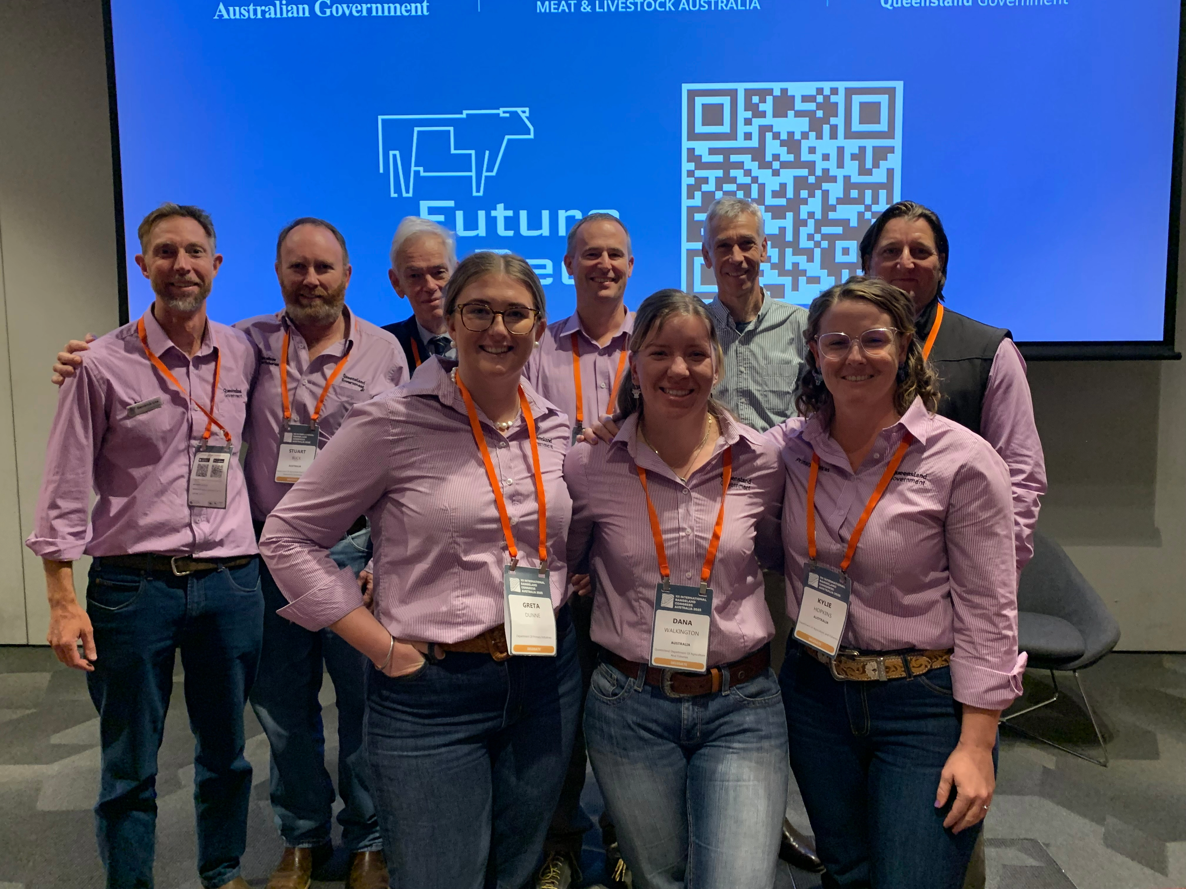 A group of DPI staff dressed in matching in shirts standing in front of a presentation screen.