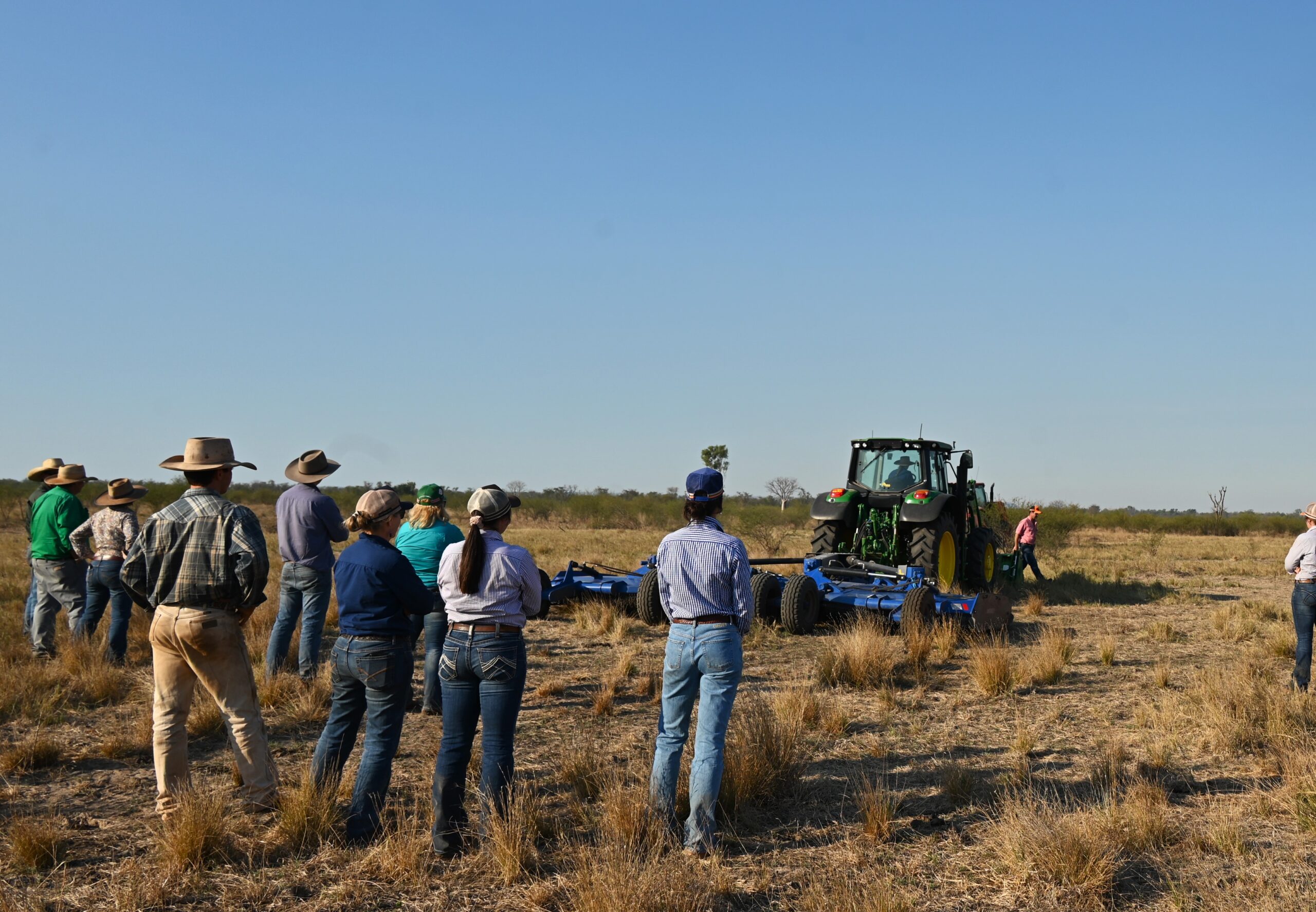Participants of the Bullo River Field Day stand in a paddock, observing a tractor in action.