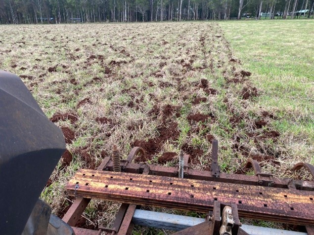 Chisel plough being pulled through pasture, leaving rip lines.