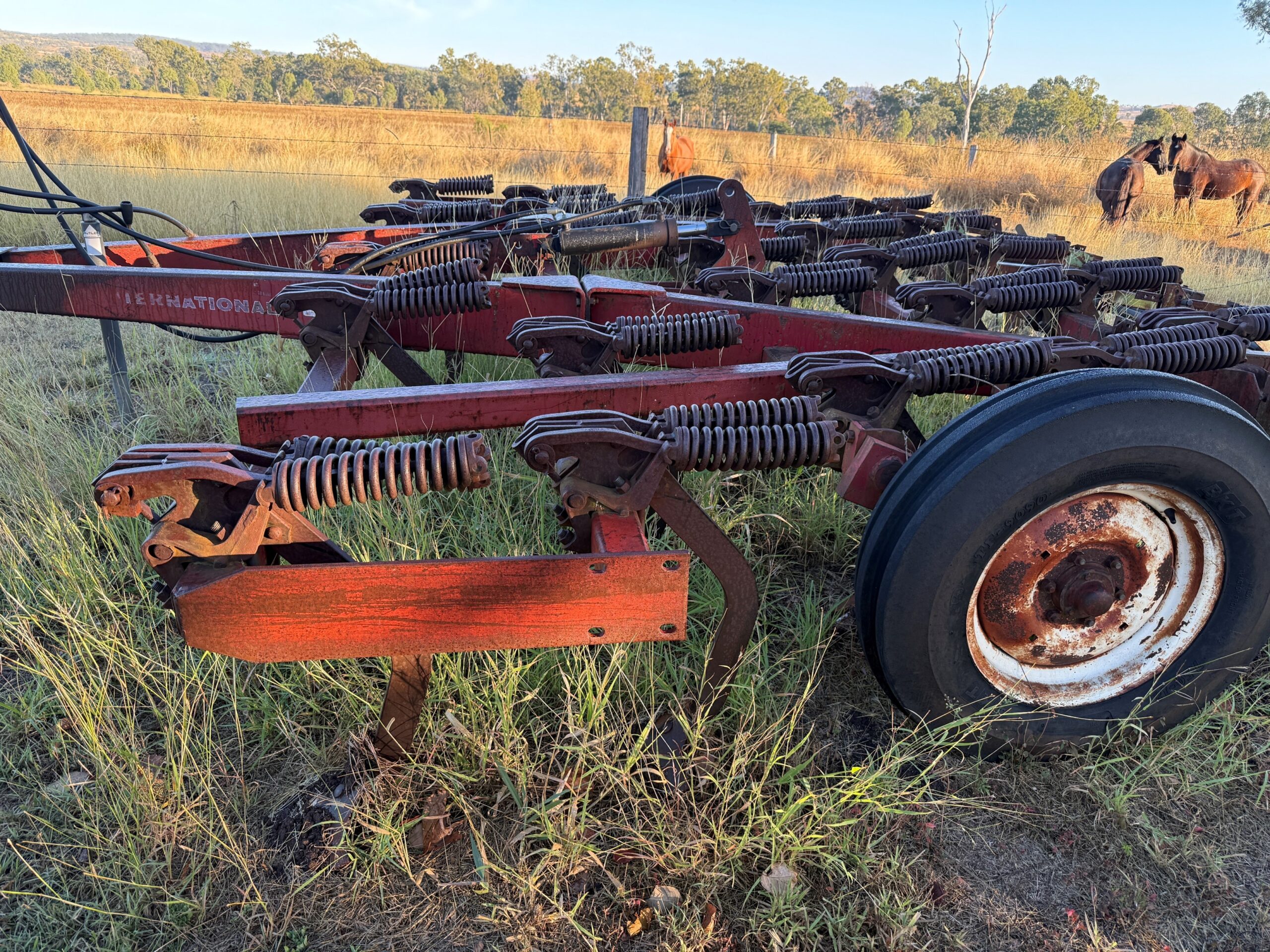 Red piece of machinery with a steel frame and spring loaded tynes.