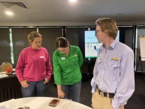 Three people standing around a table that has a container of soil dispersing in water on it.
