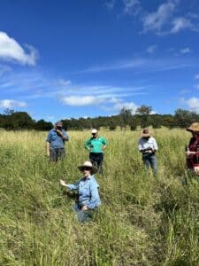 Lady crouched down in a paddock of green grass with people standing around her.